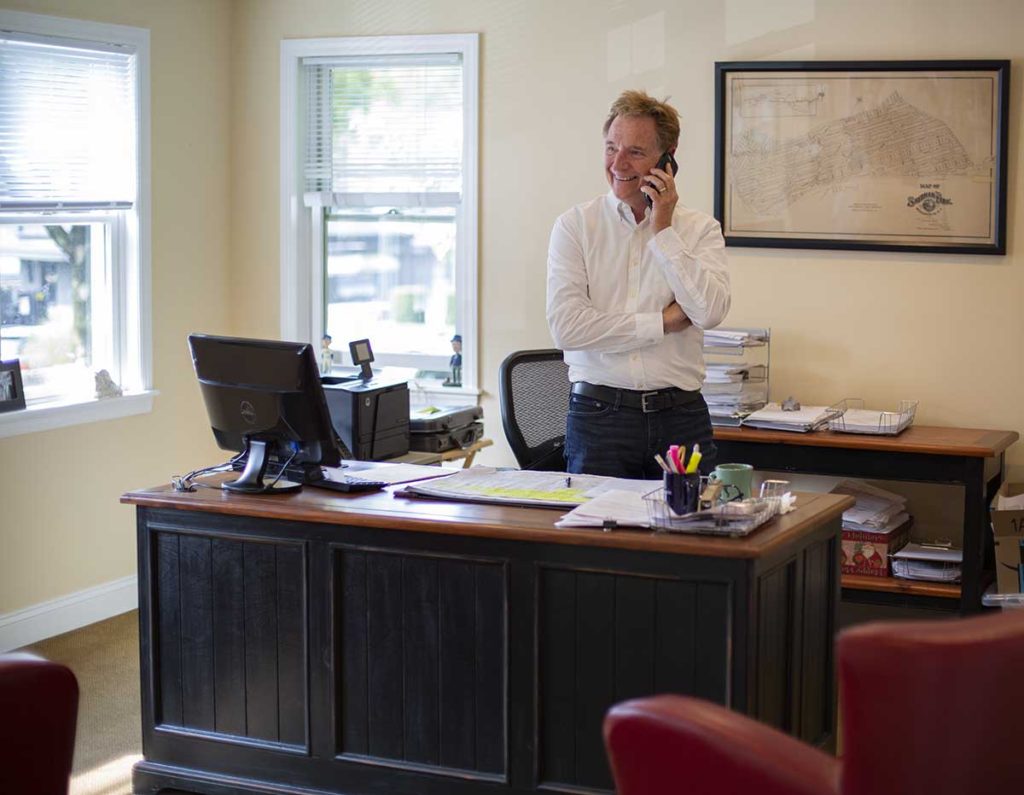 Bill McCarthy talking on phone in his office wearing white shirt and dark pants