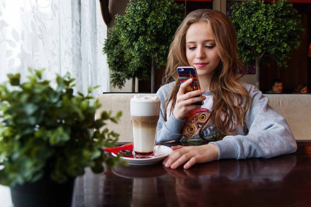 Young girl having coffee and reading smartphone