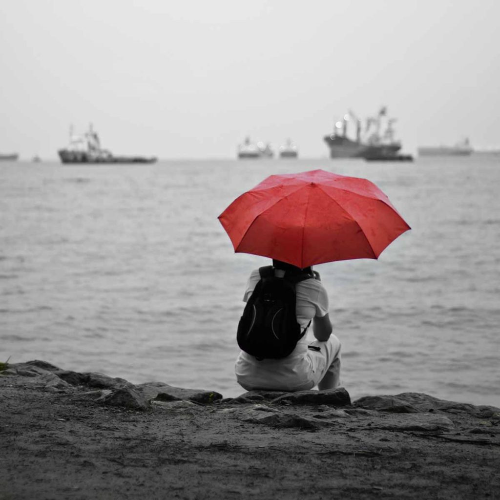 Person sitting on shore holding red umbrella